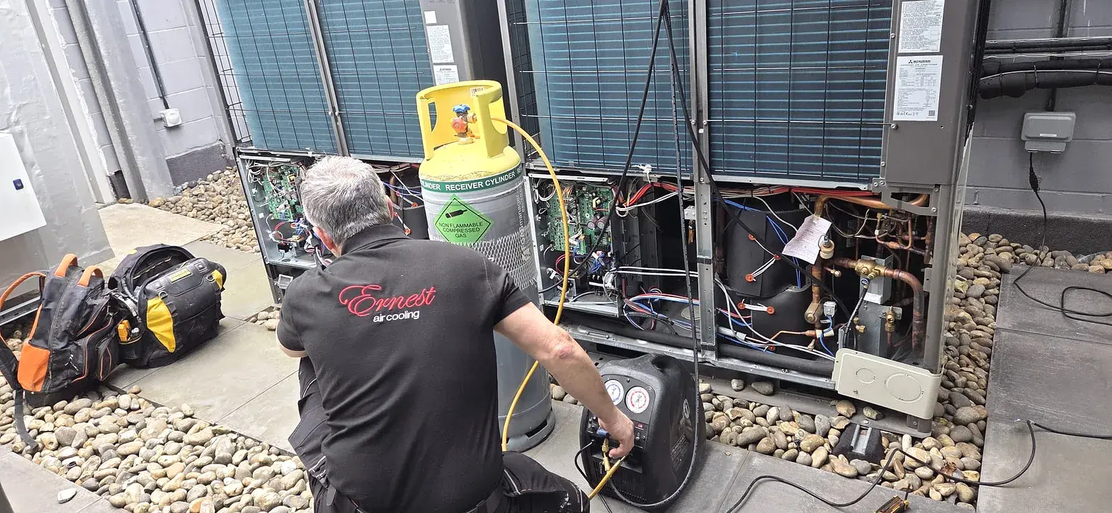 Ernest Air Cooling engineer in branded uniform servicing a Mitsubishi commercial air conditioning system on site in Sussex